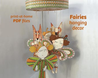 May include: A hanging mobile featuring illustrated paper figures of fairies and a fox suspended from a circular frame. The text "print-at-home PDF files" and "Fairies hanging decor" is visible. The figures have orange, green, and brown patterns.