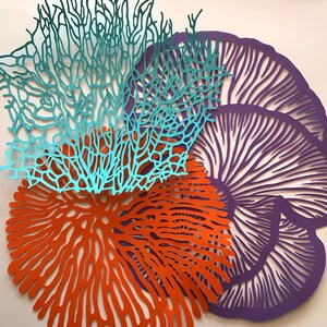May include: A collection of three flat, laser-cut decorative shapes. One piece is a teal, branching coral-like structure. Another is a bright orange, circular piece with a radial, organic pattern. The third is a purple, fan-shaped piece.