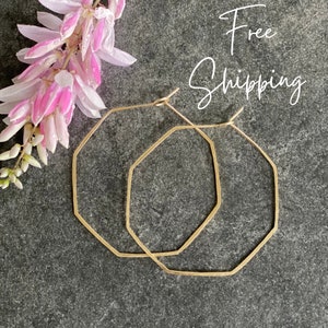 May include: A pair of gold octagon hoop earrings. The earrings are on a gray background.