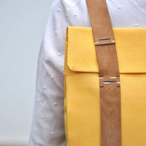 Details of a handcrafted yellow backpack. It's a close-up photo of the hand-sewn leather strap made with contrasting blue polyester threads.