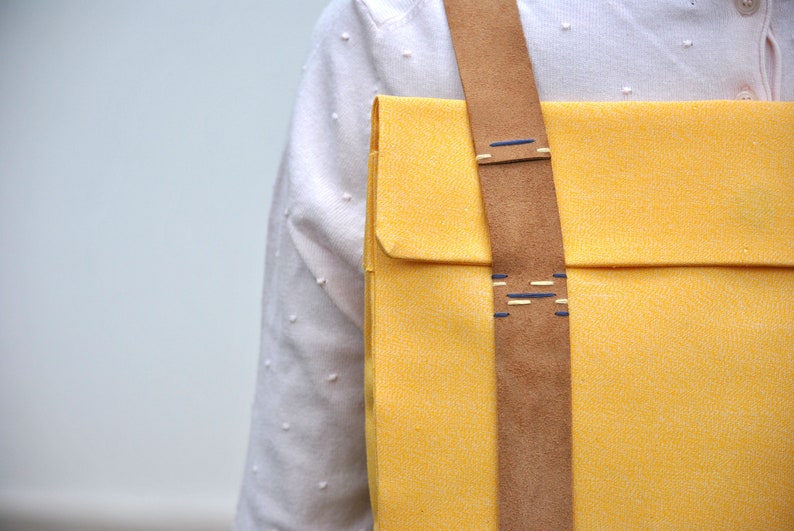 Details of a handcrafted yellow backpack. It's a close-up photo of the hand-sewn leather strap made with contrasting blue polyester threads.