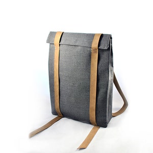 May include: A gray canvas backpack with brown leather straps. The straps are adjustable and have a buckle closure.
