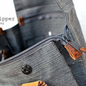 Gray backpack with zipper closure. It's written "add zipper to your bag".