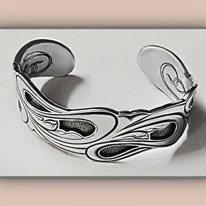 May include: A silver-toned cuff bracelet with an open design. The bracelet features an intricate pattern of flowing lines and leaf-like shapes, with textured, dark areas. The ends of the bracelet have a curved, open design.