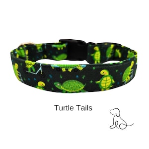 May include: A black dog collar with a green and yellow pattern of turtles. The collar has a black plastic buckle and the text "Turtle Tails" is printed below the collar.