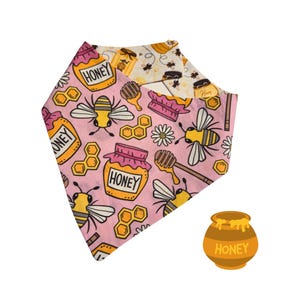 May include: Pink bandana with a bee and honey pot pattern. The bandana has a white border and the text "Honey" is repeated throughout the design.