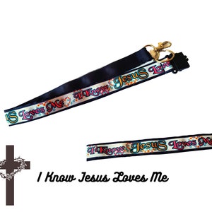 May include: A black and white lanyard with the text "I Know Jesus Loves Me" in colourful letters. The lanyard has a gold metal clasp and a black plastic swivel hook.
