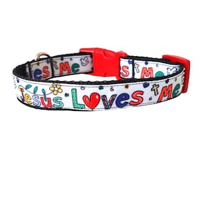 May include: White dog collar with black trim and a red buckle. The collar features a colourful design with the words "Jesus Loves Me" and a red heart.