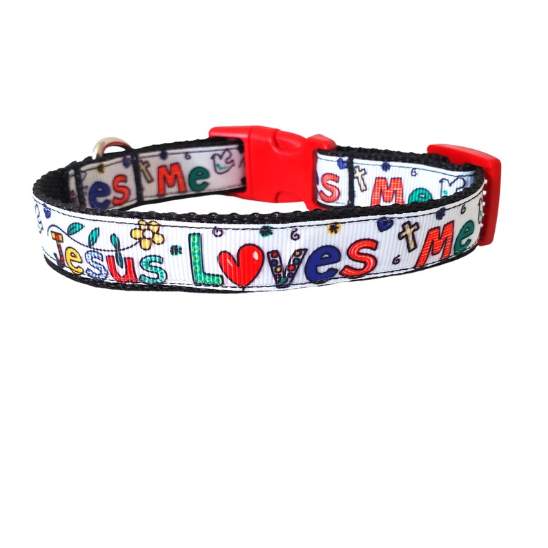 May include: White dog collar with black trim and a red buckle. The collar features a colourful design with the words "Jesus Loves Me" and a red heart.