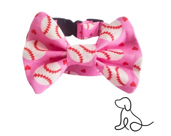 May include: A pink pet collar featuring a fabric bow tie with a repeating pattern of white baseballs with red stitching and small red hearts. The collar includes a black plastic side-release buckle and a simple black line drawing of a dog.