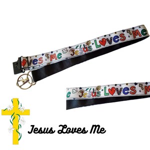 May include: White lanyard with black trim and a repeating pattern of "Jesus Loves Me" in colourful letters with a red heart. The lanyard has a metal key ring attached.