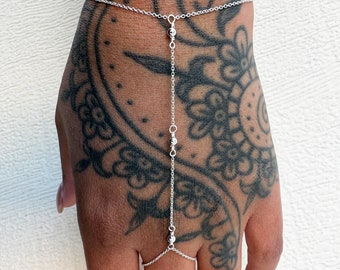 May include: A delicate silver hand chain featuring a thin cable link chain that wraps around the wrist and connects to a single ring component worn on the middle finger, accented with three small, polished silver beads along the central vertical chain.