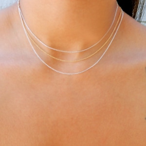May include: Three delicate gold and silver chains layered on a person's neck. The chains are all the same style, but different lengths.
