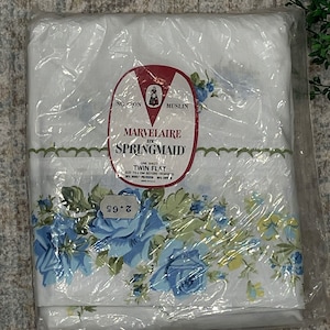 May include: A white twin flat sheet with a blue and green floral pattern. The sheet is packaged in plastic and has a red label that says "Marvelaire by Springmaid" and "NC Cron Muslin".