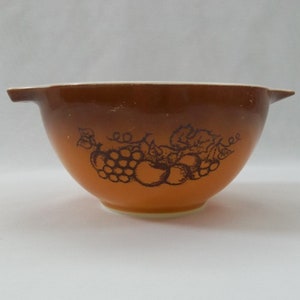 May include: A brown mixing bowl with a white rim and a black and white design of grapes and apples.