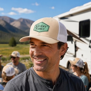 Könnte beinhalten: Eine beige-weiße Trucker-Cap mit einem hellgrünen, sechseckigen Aufnäher auf der Vorderseite. Der Aufnäher zeigt den Text THE STEVEN'S FAMILY EST 1995 in schwarzer Schrift. Die Kappe hat ein beiges Vorderteil und ein weißes Netz-Rückenteil.