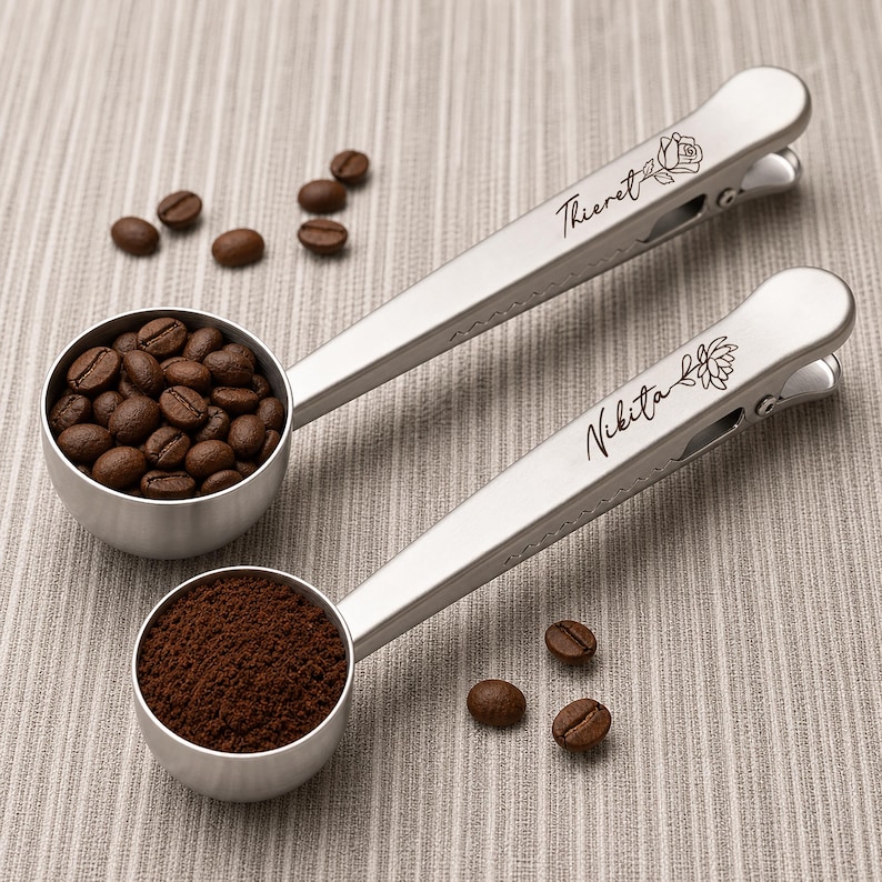 May include: Two silver-toned metal coffee scoops with integrated bag clips on the handles. One scoop is filled with whole coffee beans, and the other contains ground coffee. The handles are engraved with the names Thieret and Nikita.