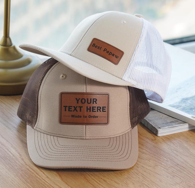 May include: Two beige and brown trucker hats with brown leather patches. The patch on the top hat says "Best Papaw". The patch on the bottom hat says "YOUR TEXT HERE - Made to Order".