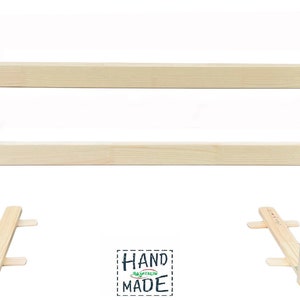 Könnte beinhalten: Ein Bettschutz aus Naturholz mit zwei horizontalen Stäben und einem kleinen grünen Aufkleber mit dem Text "HAND MADE" in der oberen rechten Ecke.
