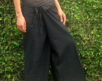 May include: Black wide-leg pants with a wrap-around waist and drawstring closure. The pants are made of a soft, flowing fabric and are suitable for casual wear. The pants are shown on a person standing on grass in front of a green hedge.