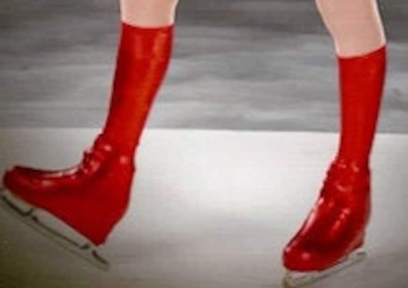 May include: A pair of red ice skates with white blades. The skates are on a white surface.