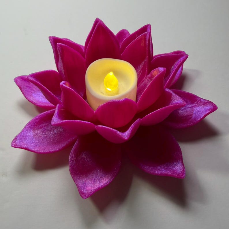 Puede incluir: Un portavelas en forma de flor de loto magenta con una vela que funciona con pilas. La vela es blanca con una llama amarilla. Los p&eacute;talos de la flor tienen una textura aterciopelada y est&aacute;n dispuestos en capas.