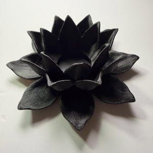 Puede incluir: Un portavelas negro con forma de flor de loto. El portavelas est&aacute; hecho de un material negro mate y tiene formas de p&eacute;talos detalladas. Un acento decorativo para la decoraci&oacute;n del hogar.