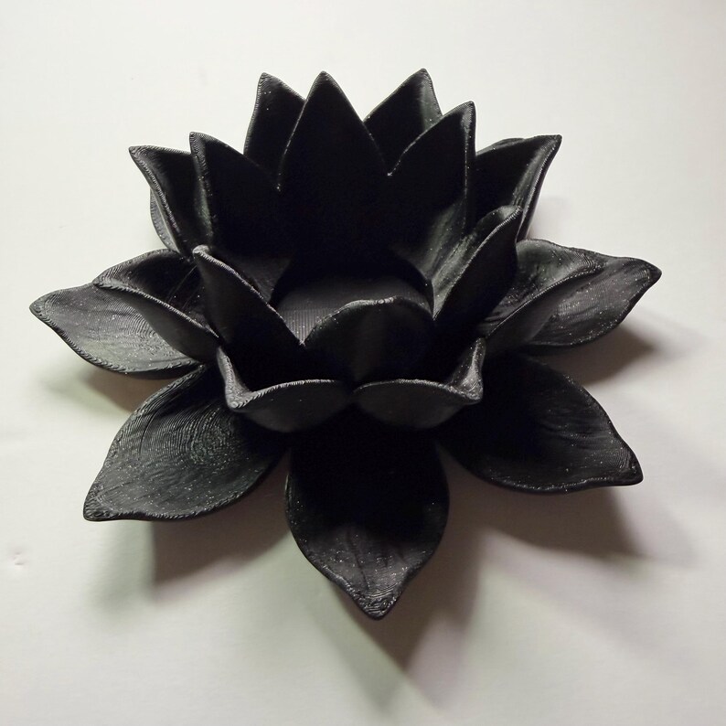 Puede incluir: Un portavelas negro con forma de flor de loto. El portavelas est&aacute; hecho de un material negro mate y tiene formas de p&eacute;talos detalladas. Un acento decorativo para la decoraci&oacute;n del hogar.