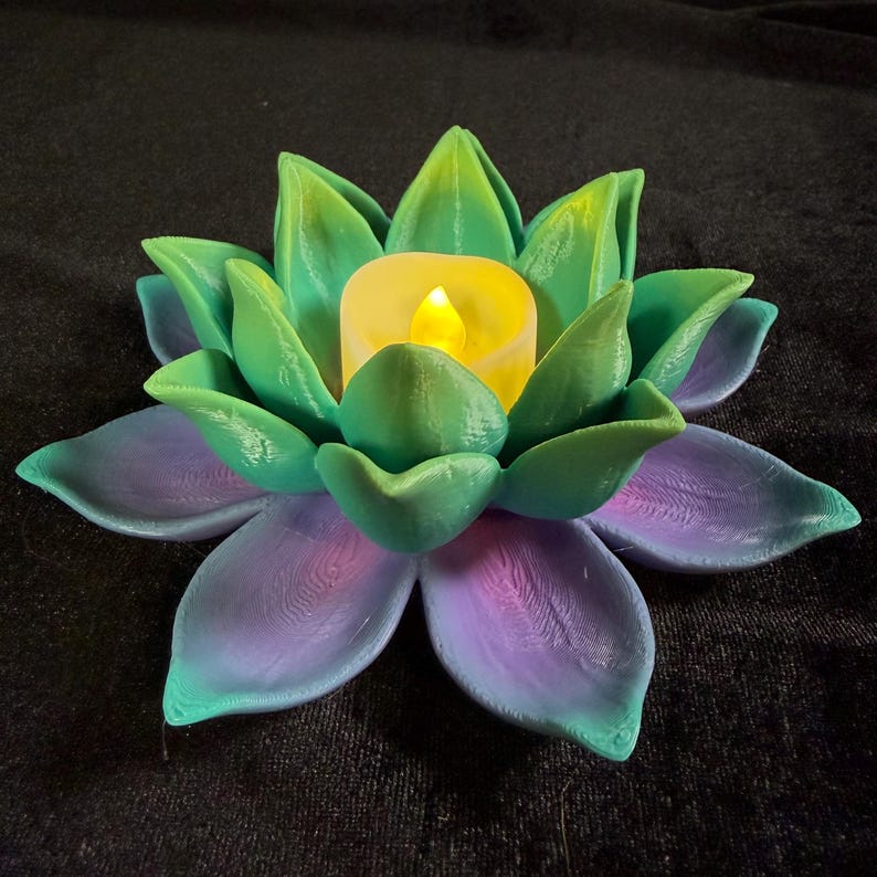 Puede incluir: Un portavelas decorativo con forma de flor de loto en tonos verdes y morados, con una vela LED amarilla en el centro. Los p&eacute;talos est&aacute;n detallados con un dise&ntilde;o texturizado, creando una pieza &uacute;nica y art&iacute;stica para la decoraci&oacute;n del hogar.
