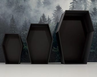 May include: Three matte black open containers shaped like coffins, arranged in a row from smallest to largest. Each container features a hexagonal silhouette with straight sides and a flat base, providing an open interior space for storage.