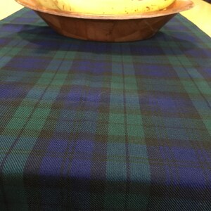 May include: A green and blue plaid table runner with a wooden bowl filled with yellow bananas on top.