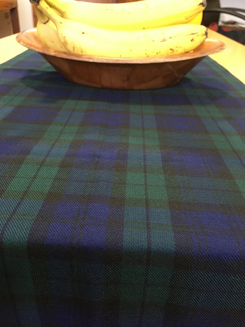 May include: A green and blue plaid table runner with a wooden bowl filled with yellow bananas on top.