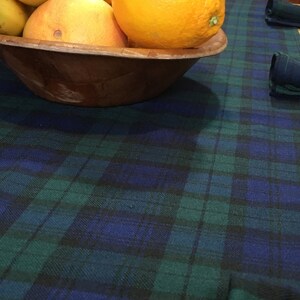 May include: A wooden bowl filled with yellow bananas and a large orange, sitting on a blue and green plaid tablecloth.