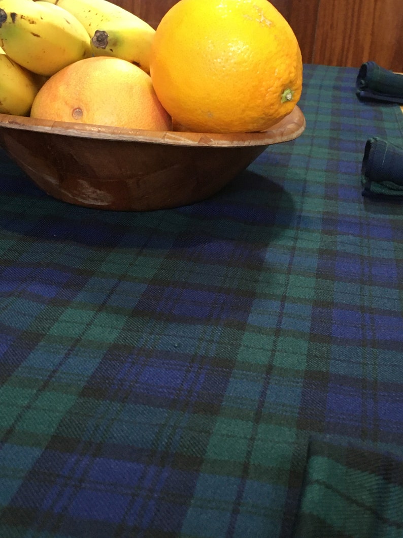 May include: A wooden bowl filled with yellow bananas and a large orange, sitting on a blue and green plaid tablecloth.