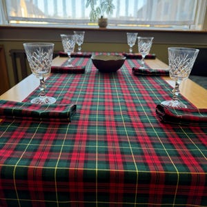 May include: A red, green and yellow tartan table runner with four clear glass wine glasses and a brown bowl on a wooden table.
