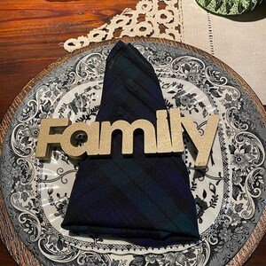 May include: A gold-colored wooden "Family" sign sits on a black and white patterned plate with a dark blue and green plaid napkin.