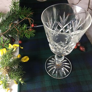 May include: Two clear glass wine glasses with a cut crystal design on a blue and green plaid table runner.