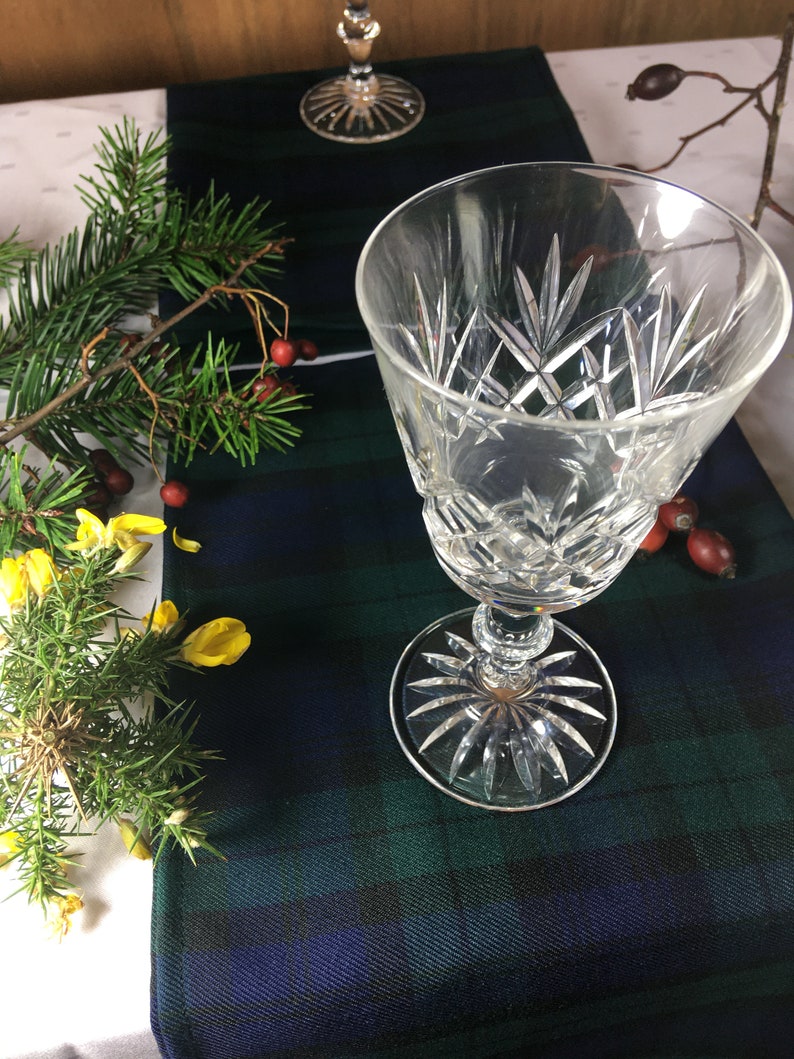 May include: Two clear glass wine glasses with a cut crystal design on a blue and green plaid table runner.