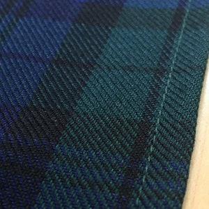 May include: Close-up of a dark green and blue plaid fabric with a white stitch along the edge.