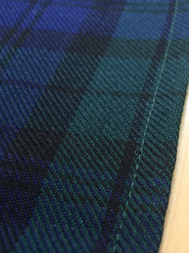 May include: Close-up of a dark green and blue plaid fabric with a white stitch along the edge.