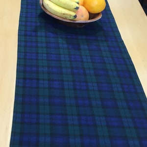 May include: A blue and green plaid table runner with a bowl of fruit on top. The bowl contains bananas and oranges.