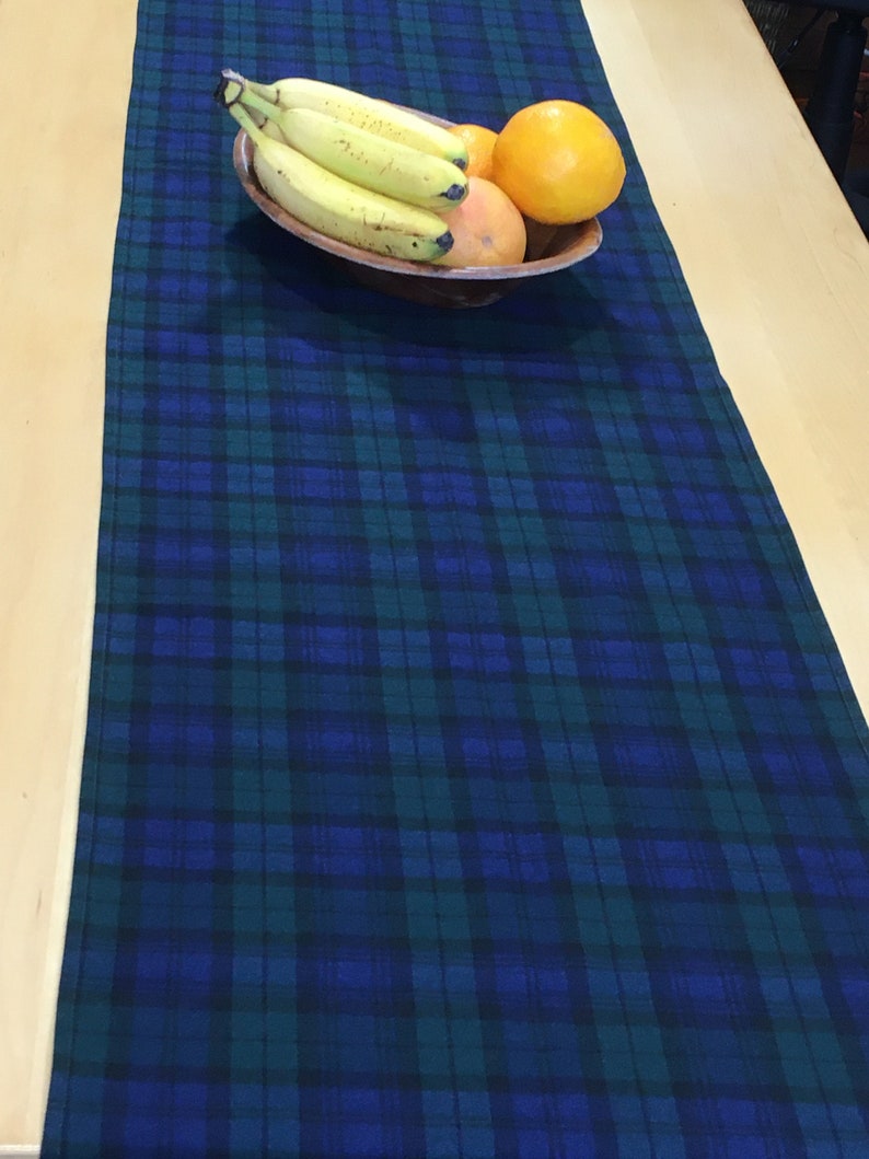 May include: A blue and green plaid table runner with a bowl of fruit on top. The bowl contains bananas and oranges.