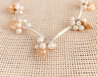 May include: A silver and gold necklace with a curved design and multiple clusters of white pearls. The necklace features several gold leaf-shaped pendants.