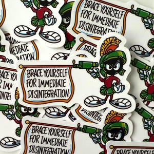 May include: A collection of stickers featuring the cartoon character Marvin the Martian. Each sticker shows Marvin holding a ray gun and a banner with the text "Brace Yourself For Immediate Disintegration". The stickers are white with colorful accents.
