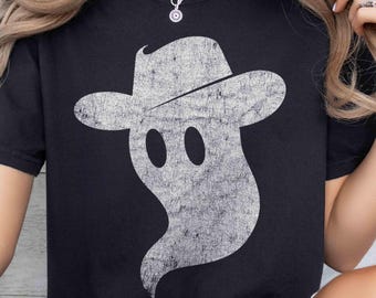 May include: A black short-sleeve t-shirt featuring a large, distressed white graphic of a ghost wearing a fedora hat. The ghost design has a textured, weathered appearance. A small black circular label in the top left corner displays the text BLACK.