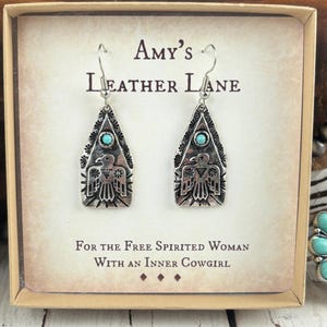 May include: A pair of silver-toned earrings with a turquoise stone and a bird design, displayed in a box. The box reads "Amy's Leather Lane" and "For the Free Spirited Woman With An Inner Cowgirl."