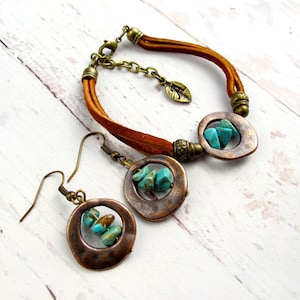 May include: A set of turquoise and copper jewelry featuring a leather bracelet with a copper circle pendant and matching earrings. The copper circles have a hammered texture and feature turquoise stones.