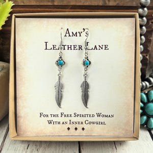 May include: Silver feather earrings with turquoise detailing, presented in a gift box. The earrings are from the "Amy's Leather Lane" collection, with the text "For The Free Spirited Woman With An Inner Cowgirl."