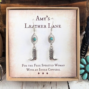 May include: Silver-toned dangle earrings featuring a small turquoise-colored stone set in an oval frame above a detailed cowboy boot charm. The earrings are displayed on a card labeled Amy's Leather Lane, For the Free Spirited Woman With an Inner Cowgirl.