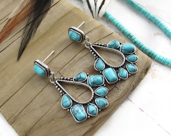 May include: A pair of silver-toned drop earrings featuring a teardrop-shaped frame accented with twisted metal detailing and multiple inlaid turquoise-colored stones with dark veining. Each earring includes a single rectangular stone stud top.